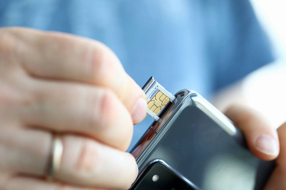 Mężczyzna trzyma w dłoni swój telefon, a za pomocą drugiej ręki próbuje wyciągnąć tackę z zablokowaną kartą SIM.